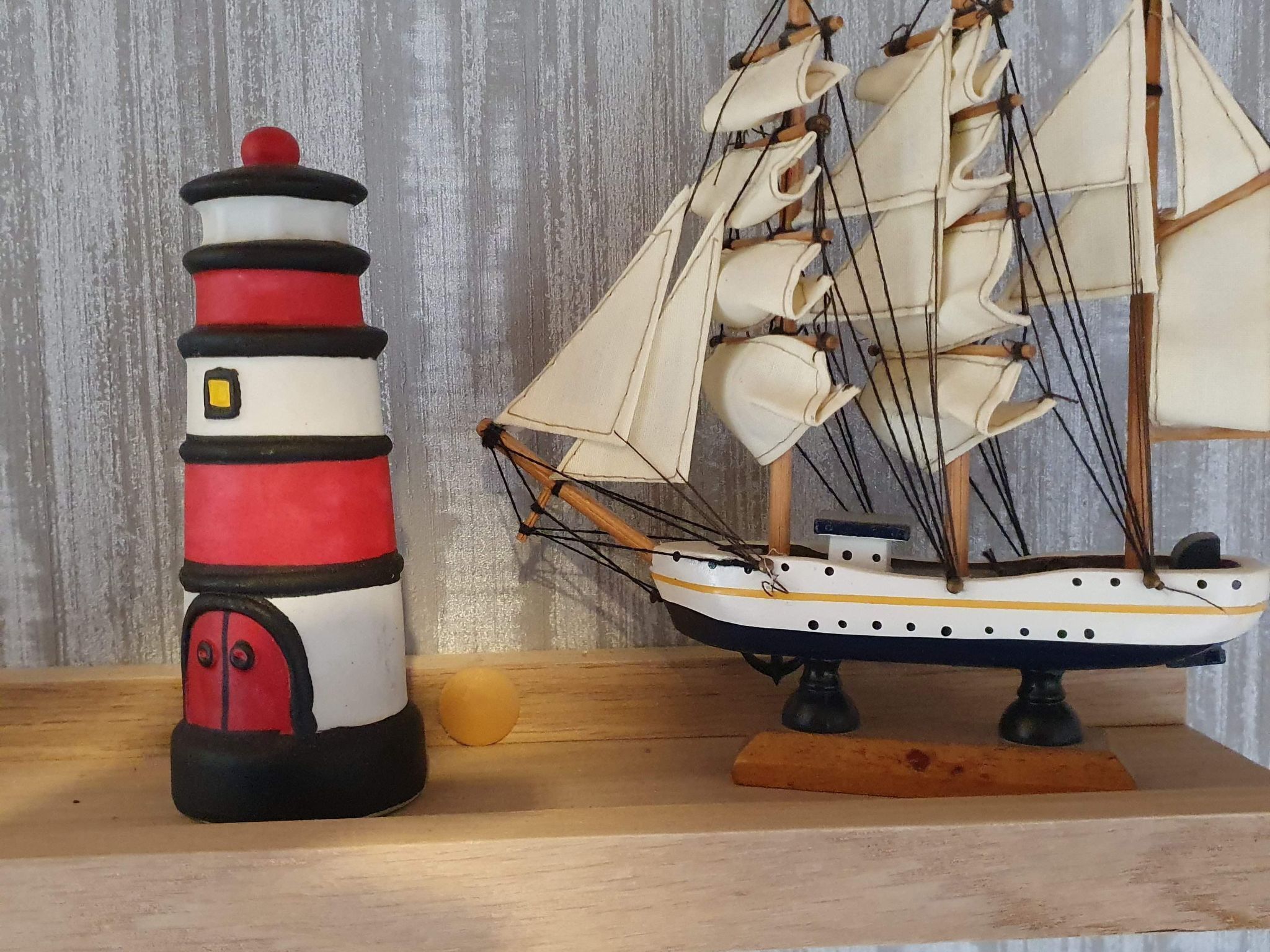 A lighthouse and a model sailing ship on a wooden shelf.