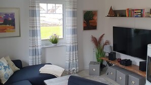 Una sala de estar con un sofá, un televisor, una estantería y una ventana con cortinas.