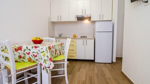 A compact kitchen with white cabinets, a white refrigerator, and a dining table with a fruit-patterned tablecloth. - Wohnung in Stoja mit Grill by Interhome (Pula)