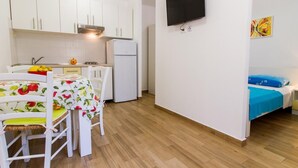 A compact room with a kitchenette, a bed with a blue bedspread, and a wall-mounted TV. - Wohnung in Stoja mit Grill by Interhome (Pula)