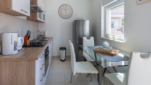 Eine kompakte Küche mit Holzausziehtisch, Edelstahlgeräten, einem Glastisch und Blick durch ein Fenster nach draußen.