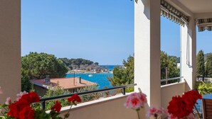 Ein Balkon mit Meerblick, roten Blumen und einem Ziegeldach im Hintergrund.