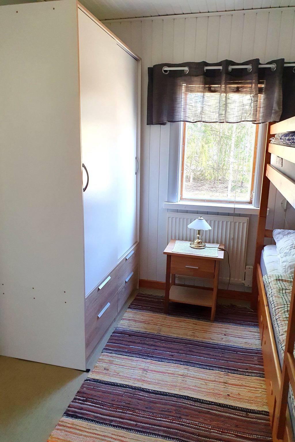 Une petite pièce agréable, dotée d’un lit superposé, d’un bureau avec une lampe, d’une fenêtre avec des rideaux et d’un radiateur.