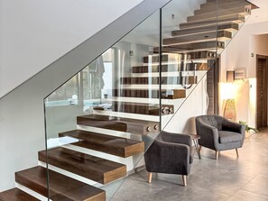 A modern staircase with glass railings and wooden steps, a grey armchair, and a lamp in a contemporary living area. - Villa Velika by Interhome (Bokordici)