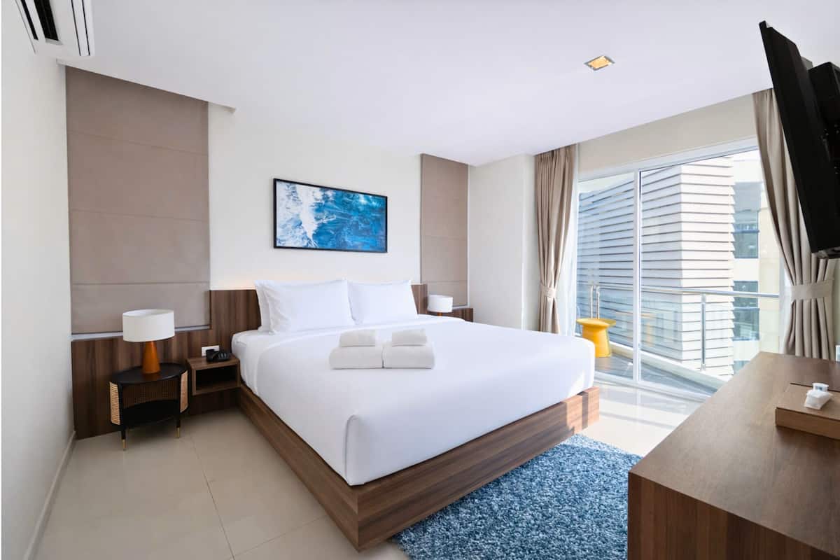 A modern hotel room with a large bed, a flat-screen TV, a desk, and a view of the city.