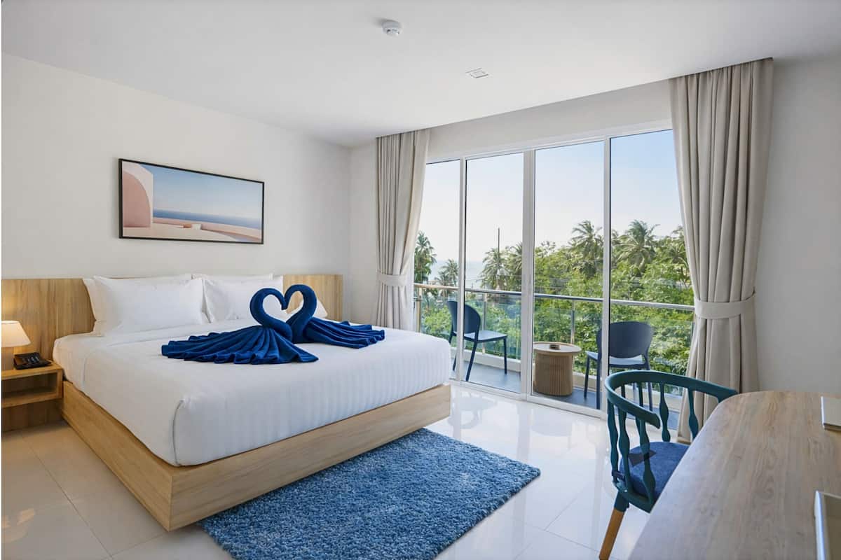 A modern hotel room with a large bed, a balcony with a view, and a painting on the wall.