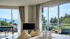 A hotel room with a large bed, a flat-screen TV, a balcony with chairs, and a view of the ocean and palm trees. - Aqua Maya Phuket (Patong)