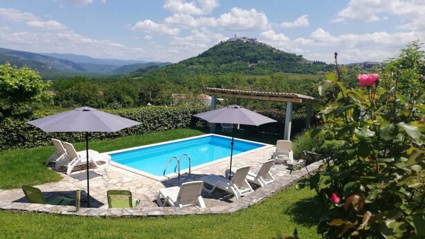 A swimming pool with lounge chairs and umbrellas, surrounded by a grassy lawn and a view of a hill with buildings in the distance. - "Valentino" mit Blick auf das Wasser by Interhome (Motovun)