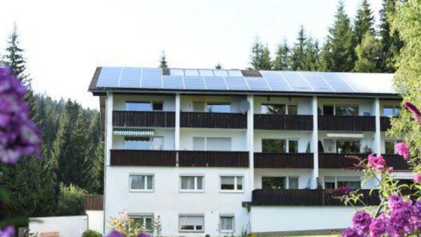 A multi-story building with a flat roof covered in solar panels, surrounded by greenery and flowering plants. - in Frauenberg mit Garten by Interhome (Haidmühle)