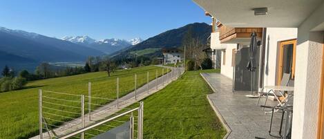 A residential property with a balcony overlooking a green field and mountains.