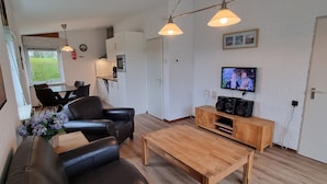 A modern living room with a sofa, coffee table, and TV. There is a kitchen area with cabinets and a dining table. - Gemütliches Ferienhaus De Blenck by Interhome (Callantsoog)