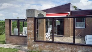 A modern house with a brick exterior, large glass windows, and a red awning. - Gemütliches Ferienhaus De Blenck by Interhome (Callantsoog)