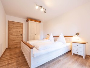 A bedroom with a wooden floor, a white bed with two pillows, a wooden wardrobe, and a bedside table with a lamp. - mit Terrasse und zwei Schlafzimmer by Interhome (Breitenberg)