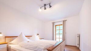 Une chambre à coucher avec un lit en bois, une literie blanche, une table de chevet, une lampe de chevet, un luminaire au plafond et une fenêtre avec des rideaux.
