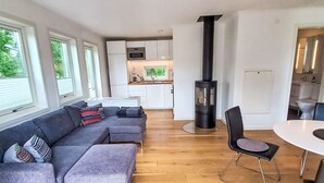 A modern living space with a sofa, ottoman, dining table, chairs, a kitchen area, and a wood-burning stove. - Ljugarn 2 by Interhome (Ljugarn)