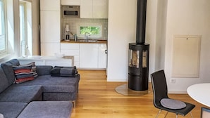 A modern living room with a sofa, a dining table, and a kitchen area with white cabinets and a black stove. - Ljugarn 2 by Interhome (Ljugarn)