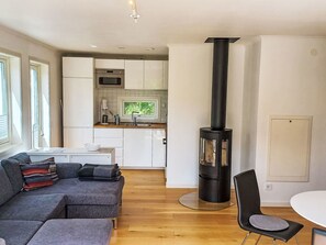 A modern living room with a sofa, a dining table, and a kitchen area with white cabinets and a black stove. - Ljugarn 2 by Interhome (Ljugarn)