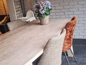 A dining area with a long wooden table, woven chairs, and a wicker basket with flowers. - Gemütlicher Bungalow für 4 Personen by Interhome (Callantsoog)