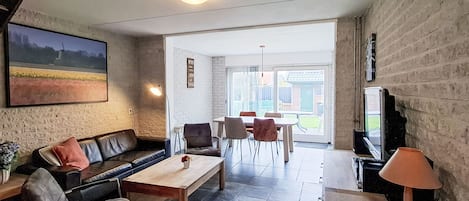 A living room with a sofa, coffee table, and chairs, a television, and a view of the outdoors.