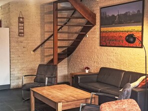 A modern living room with a wooden staircase, a sofa, a coffee table, and a painting on the wall. - Gemütlicher Bungalow für 4 Personen by Interhome (Callantsoog)