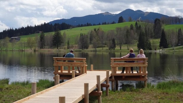 Une jetée en bois s’étendant sur un lac paisible, avec des montagnes en arrière-plan.