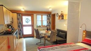 Une chambre d’hôtel compacte comprenant un coin cuisine, un espace repas et un lit avec une literie à motifs floraux.