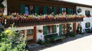 Un bâtiment traditionnel doté d’un balcon orné de fleurs aux couleurs vives, d’un banc en bois et d’une cour pavée.