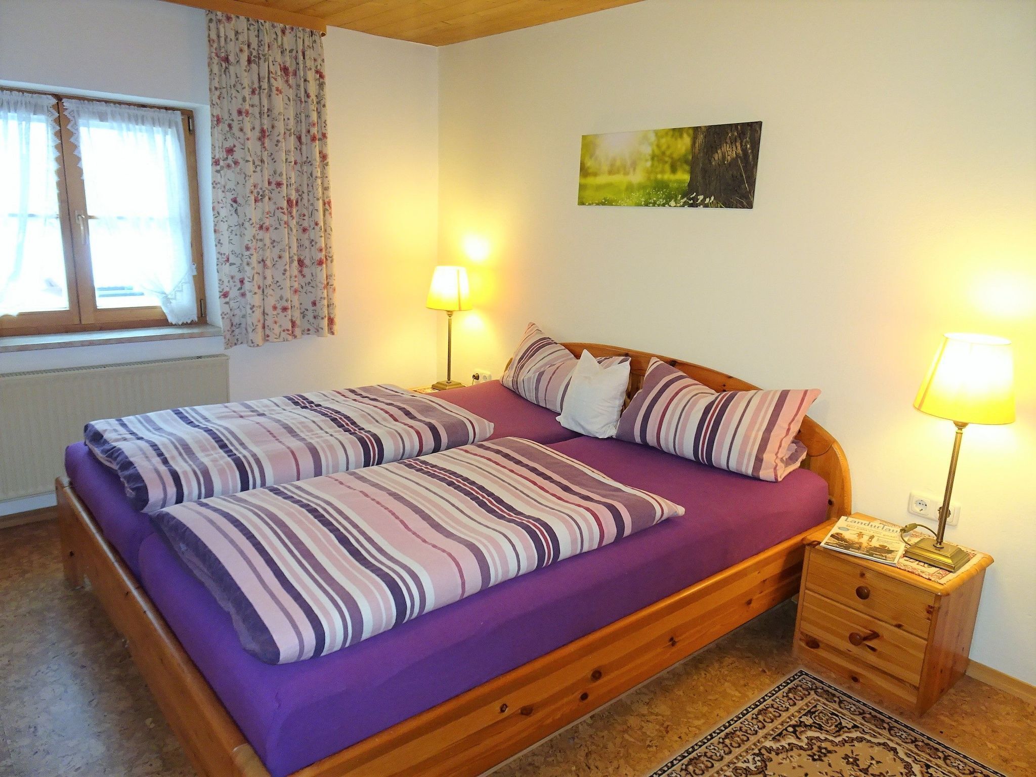 A double bed with striped bedding, a wooden headboard, bedside lamps, a small wooden nightstand, and a framed picture on the wall.