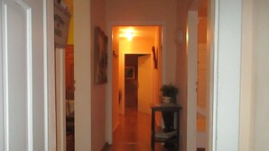 Un couloir étroit avec un plancher en bois, une petite table sur laquelle est posée une plante, et une porte au fond.