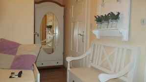 Une chambre à coucher avec un lit, un banc blanc, un miroir et une étagère avec des plantes.