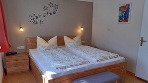 Uma cama de casal com um banco aos pés, uma mesinha de cabeceira e uma decoração na parede com estrelas e texto.