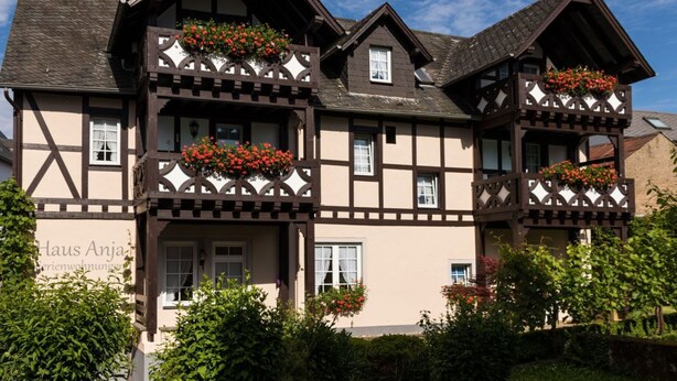 Uma casa tradicional em estilo de enxaimel, com várias varandas decoradas com flores vermelhas.