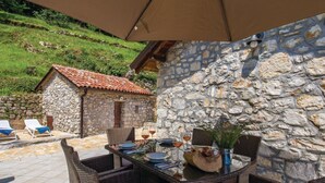 Eine Terrasse im Freien mit Korbmöbeln, einer Steinmauer und einem kleinen Steinhaus im Hintergrund.