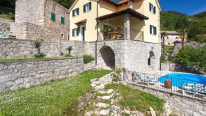Ein Steinhäuschen mit Pool, umgeben von viel Grün und Hügeln.