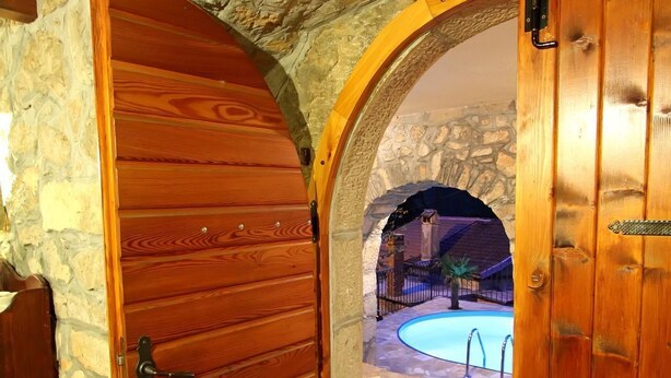 Eine Holztür führt zu einem Poolbereich mit Steinmauern und Steinboden.