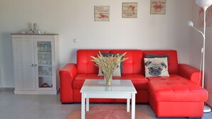Una sala de estar con un sofá rojo, una mesa de centro blanca y un aparador con puertas de vidrio. Hay tres adornos en la pared encima del sofá.