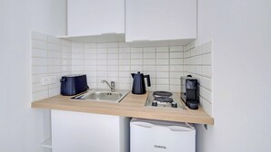 Ett kompakt kök med vita kakelplattor, en diskho, en vattenkokare, en kaffebryggare och en liten diskmaskin.