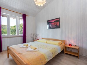 Ein Schlafzimmer mit Bett, Nachttisch, einem Gemälde und einem Fenster mit Vorhängen.