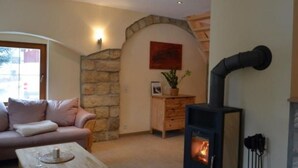 Ein gemütliches Wohnzimmer mit Steinwand, einer Couch, einem Couchtisch und einem Kaminofen.