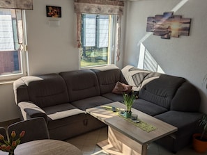 A living room with a sectional sofa, a coffee table with decorative items, a window with curtains, and a wall-mounted artwork. - mit Garten, Grill und Terrasse by Interhome (Jessern)