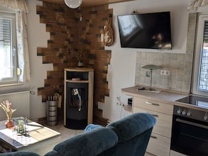 A modern kitchen with a flat-screen TV, a built-in oven, and a dining area with a table and chairs. - mit Garten, Grill und Terrasse by Interhome (Jessern)