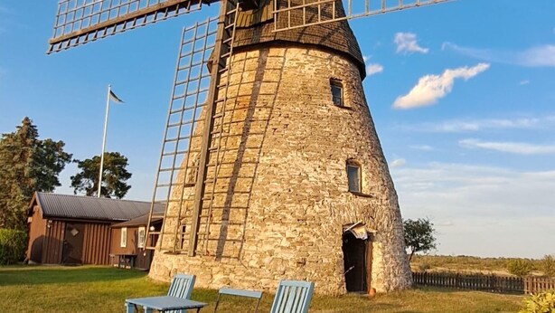 A stone windmill with a large wooden structure, two blue chairs, and a grassy field. - Karlsson by Interhome (Fågelfors)