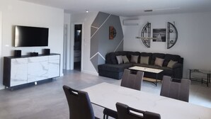 Una sala de estar moderna con un televisor de pantalla plana, un sofá de color oscuro, una mesa de comedor con sillas y una decoración minimalista.
