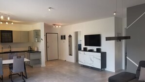Una sala de estar moderna con un sofá, un televisor montado en la pared y una zona de comedor con sillas y una mesa.