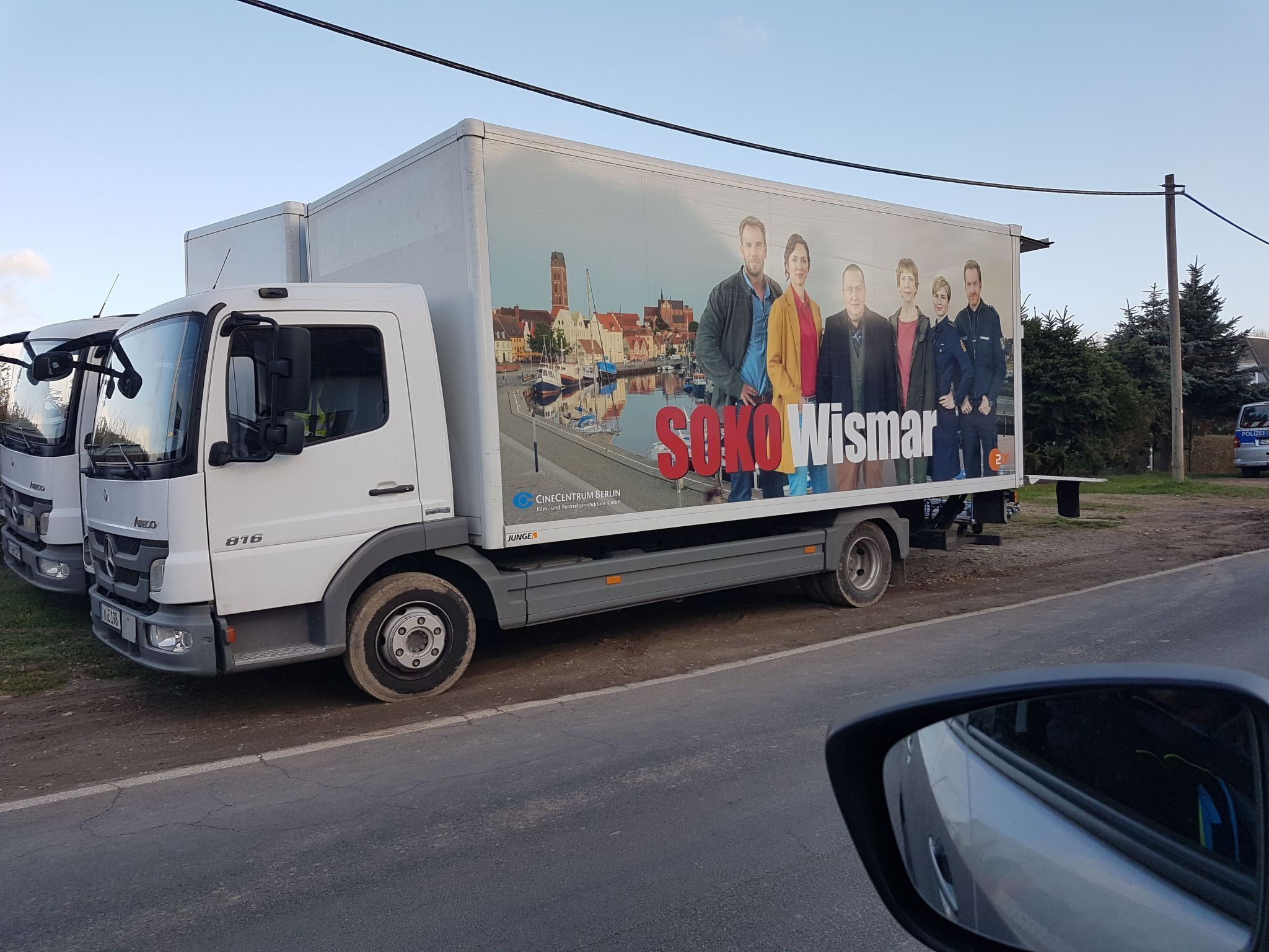 A white truck with a movie poster advertising 'Soko Wismar' parked on the side of a road.
