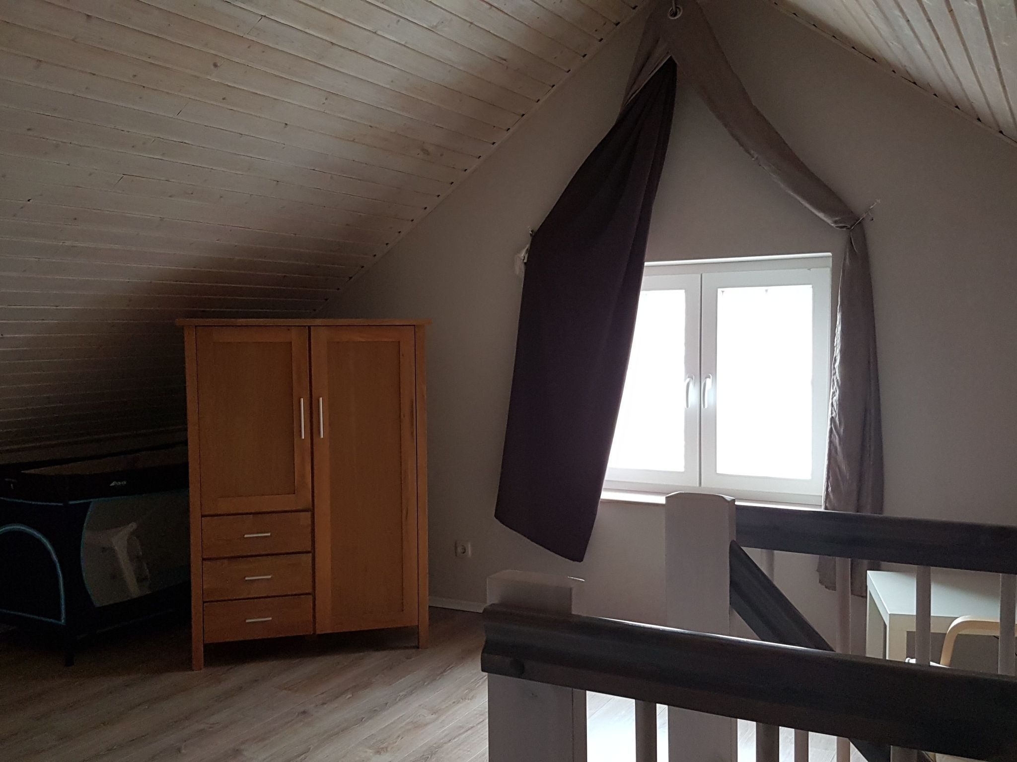 Ett rum med ett sluttande tak, en trägarderob och ett fönster med gardiner.