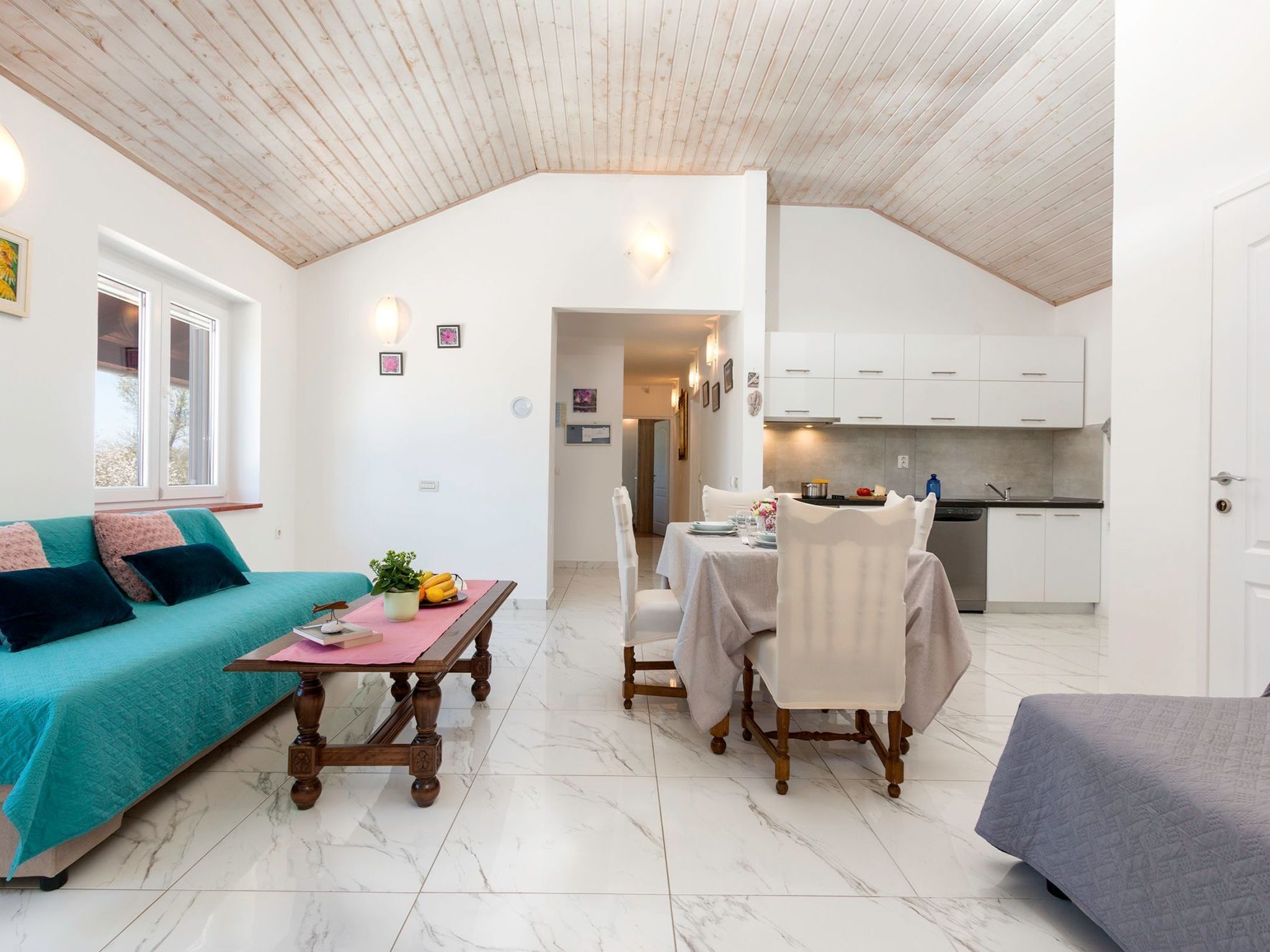 A compact living space with a dining area, kitchenette, and a cozy seating area with a teal sofa and a wooden table.