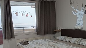 Et soveværelse med seng, et vindue med gardiner, en radiator, et sengebord med lampe og en vægdekoration.