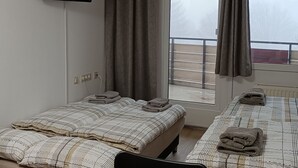 Et hotelværelse med to senge, et fjernsyn ophængt på væggen og udsigt til en balkon med gelænder.