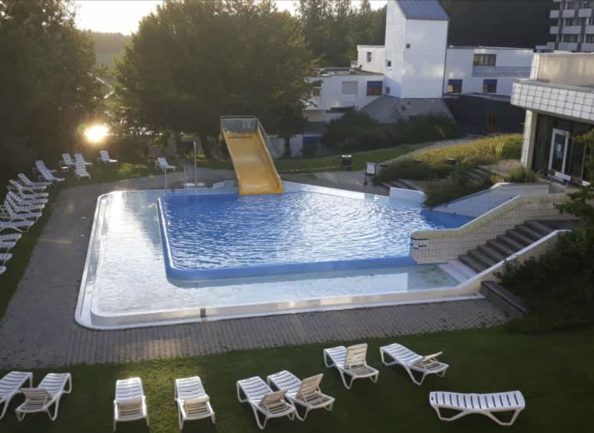 Ein Schwimmbecken mit Rutsche, umgeben von Liegestühlen und einem Gebäude.